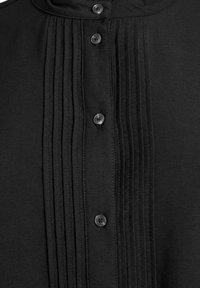 Svart skjorta med en framplagg med sex knappar, smala veck och en mjuk textur. Enkel krage utan synliga mönster.