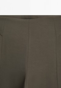 Nahaufnahme eines braunen Stoffs mit vertikalen Nähten und Steppdetails, die einen Teil eines Kleidungsbunds zeigen.