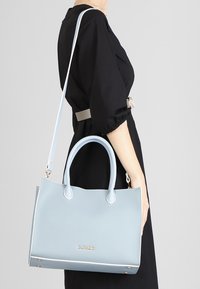 Borsa a tracolla in pelle blu chiaro con manici doppi, accessori in argento e dettagli di cucitura sottili. Include una tracolla rimovibile.