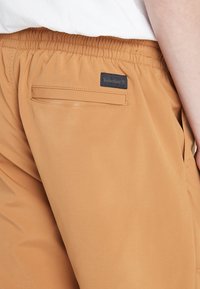 Katoenen kaki broek met een elastische tailleband, voorzien van een achterzak en een zwart Timberland-logo patch. Gladde textuur en casual pasvorm.