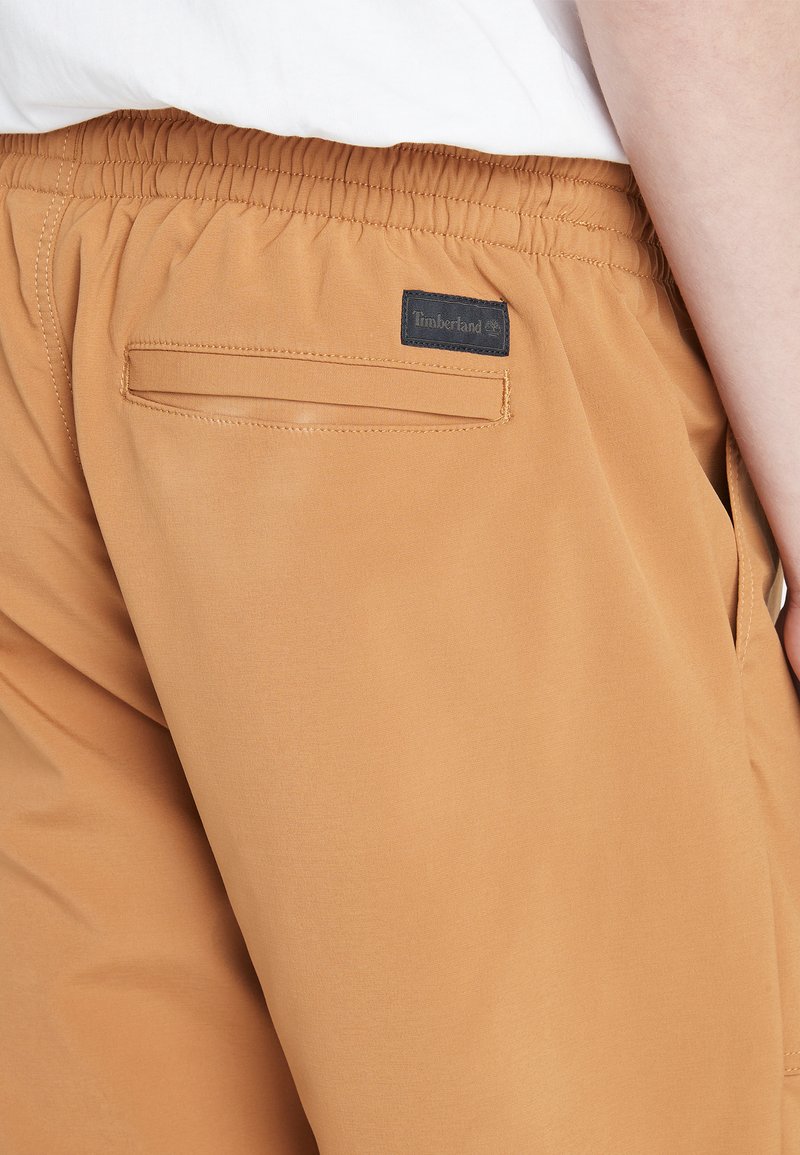 Beige Baumwollhosen mit elastischem Bund, ausgestattet mit einer Gesäßtasche und einem schwarzen Timberland-Logo-Patch. Glatte Textur und lässige Passform.