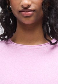 Sweat-shirt rose avec un col rond, une texture douce et des accents côtelés subtils au niveau du col. L'arrière-plan est flou.