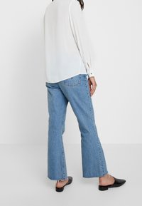 Blusa bianca a maniche lunghe con polsini abbottonati abbinata a jeans svasati azzurri. Scarpe slip-on nere con motivo a rilievo.