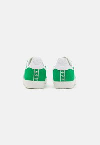 Green suede sneakers with white accents, featuring a textured rubber sole, heel tab, and three-stripe logo detail on the back.