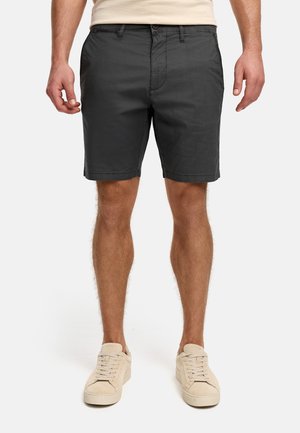 Shorts en coton gris foncé avec une fermeture à bouton et zip, poches latérales et coupe droite. Portés avec des baskets en daim beige.