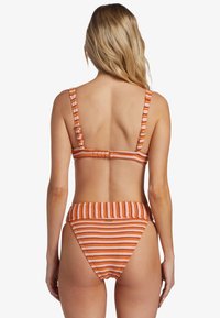 Bikini rayé orange et blanc, avec de larges bretelles, un dos avec agrafes, et un bas taille haute avec une taille froncée.