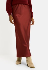 Falda maxi de satén burdeos con cinturilla elástica, textura suave y largo hasta el tobillo, combinada con botas de tacón beige.