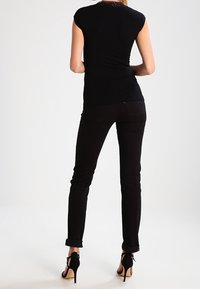 Černý přiléhavý top s krátkými rukávy spárovaný s černými skinny džíny. Oblečení má krajkový detail na dekoltu a podpatkovou obuv.
