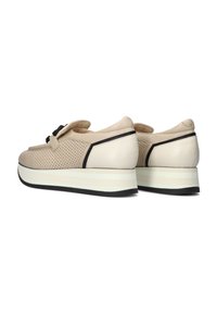 Beige leren schoenen met geperforeerde textuur, zwarte accenten en een dikke witte tussenzool. Beschikt over een afgeronde hak en een decoratieve strik.