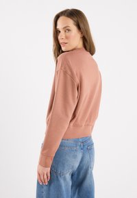 Rosa farget croppet sweatshirt med ribbede mansjetter og hem, parret med lyseblå vide denimjeans som har baklommer.