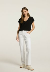 Czarna bluzka z krótkim rękawem i dekoltem w serek, zestawiona z białymi prostymi dżinsami. Posiada luźny krój i miękką fakturę. Jasnokolorowe sneakersy.