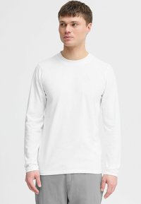 Langarm weißes T-Shirt aus weicher Baumwolle, mit rundem Halsausschnitt und schmalen Ärmeln, kombiniert mit hellgrauen Hosen.
