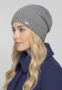 Graue, gerippte Mütze mit weicher Strickstruktur und kleinem Logoetikett. Wird mit einem marineblauen Mantel getragen und betont den lässigen Stil.