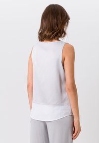 Helles graues ärmelloses Oberteil aus glattem Stoff, mit einem abgerundeten Saum und einer weißen Schicht darunter sowie einem lockeren Schnitt.