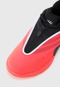 Baskets de sport rouge vif avec fermeture éclair noire et bord blanc, dotées d'une semelle texturée et de petits pois noirs sur le tissu supérieur.