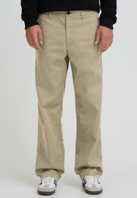 Khaki-püksid sirge säärejoonega, valmistatud puuvillasegust kangast. Omavad nööpidega sulgemist ja esimesi taskuid. Kannan valgete ja hallide tossudega.