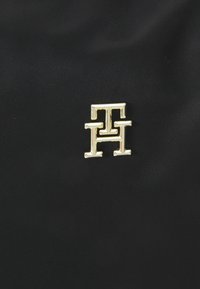 Złote metaliczne logo "TH" na czarnym teksturowanym tle, wyśrodkowane i wyraźnie widoczne.