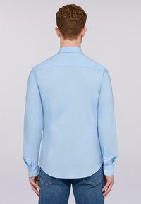 Ljusblå långärmad skjorta med rak bak, knappmanchetter och rundad nederkant. Tillverkad av ett glatt tyg med subtil struktur.