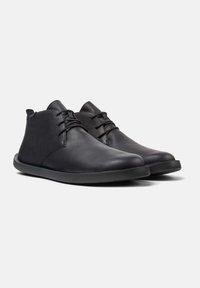 Bottines en cuir noir avec une texture lisse, bout rond et un laçage minimal. Elles sont dotées d'une semelle en caoutchouc noir pour une adhérence et une stabilité optimales.