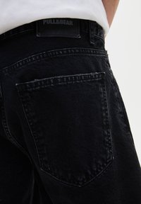 Jean en denim noir avec une coupe slim, dotés d'une poche arrière visible, de coutures décoratives et d'une patch en cuir avec le logo Pull & Bear à la taille.