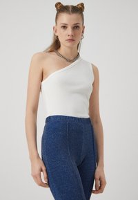 Hvit en-skulder ribbestrikket topp kombinert med blå stretchy bukser med en subtil glitring. Topp har en tettsittende passform; buksene har strikk i livet.