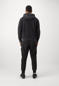 Zwarte hoodie met een gestructureerde afwerking, voorzien van een trekkoordcapuchon en ribgebreide manchetten. Gecombineerd met slim-fit zwarte broek en zwarte sportschoenen.