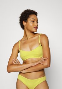 Conjunto de bikini amarelo com tecido texturizado, apresentando um top bralette com alças ajustáveis e uma parte de baixo hipster a condizer. Design simples e justo.
