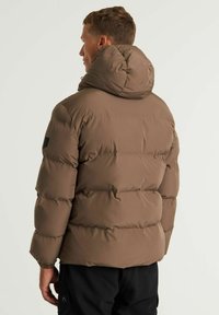 Chaqueta de plumas marrón con cuello alto, diseño acolchado y textura suave. Cuenta con puños elásticos y un parche con el logo en la manga.
