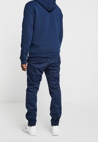 Felpa blu navy con tasca frontale a marsupio, orlo a coste e pantaloni abbinati. Tessuto morbido con polsini elasticizzati e vestibilità rilassata.