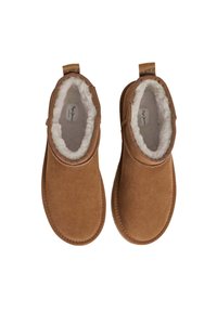 Stivaletti alla caviglia in suede marrone con una morbida fodera in pelliccia bianca e linguette posteriori, caratterizzati da un design semplice e arrotondato.