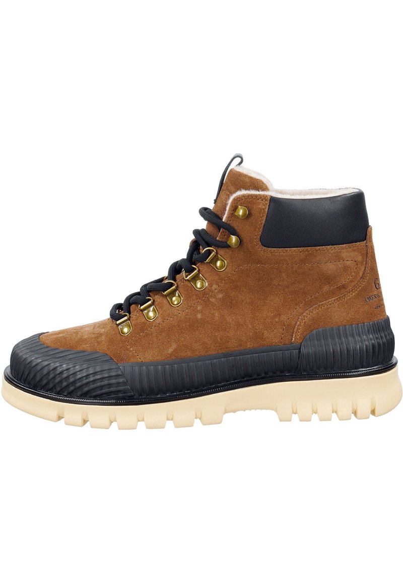 Brauner Wildlederstiefel mit einer schwarzen Gummispitze und Zwischensohle, ausgestattet mit schwarzen Schnürsenkeln, goldenen Ösen und einer strukturierten cremefarbenen Außensohle.