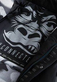 Schwarze Jacke mit einem silbernen Grafikdruck eines Gorilla-Gesichts, dem Text "#CONNECTED" und dem Etikett "SYSTEM-REBOOT 1000" im Innenfutter.