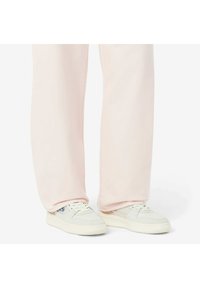 Un pantalon de survêtement rose clair avec une coupe ample, présentant une texture lisse et un design simple, associé à des baskets blanches avec une semelle texturée.