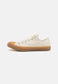 Cream canvas sneaker with a round, tan rubber toe cap and gum sole. Features white laces and metal eyelets. Simple, low-profile design.