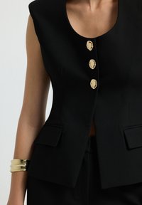 Gilet nero su misura con scollatura rotonda, dotato di tre bottoni color oro e due tasche laterali. Tessuto liscio con una vestibilità strutturata.
