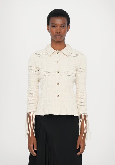 Elfenbeinfarbene Strickjacke mit Kragen, Knopfverschluss und offener Webstruktur. Besitzt fransige Ärmel und eine taillierte Silhouette.
