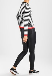 Zwart-wit gestreepte trui met rode accenten, gecombineerd met zwarte skinny broek en zwarte sneakers. De outfit heeft een casual, aansluitend ontwerp.