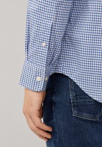 Camisa de cuadros azul y blanca con puños abotonados, que presenta una suave textura de algodón, combinada con jeans de denim oscuros.