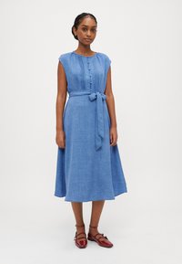 Rochie albastră, fără mâneci, cu talie îmbelătată, din material texturat, cu detalii cu nasturi pe față; asortată cu pantofi plat roșii.