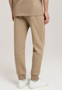 Beżowe bawełniane joggery z prążkowanymi mankietami, bocznymi kieszeniami i kieszenią z tyłu. W połączeniu z białymi tenisówkami. Gładka faktura i luźny krój.