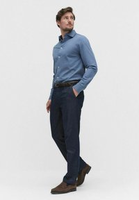 Lichtblauwe overhemdd met lange mouwen, gecombineerd met donkerblauwe broek en bruine suède schoenen, met een gestructureerde zwarte riem.
