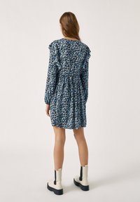 Musta kukkamekko sinisten ja kermaisten kuvioiden kanssa, frilliyksityiskohdat olkapäillä, kerätty vyötärö, ja yhdistetty vaaleanbeigeihin nilkkabootseihin.