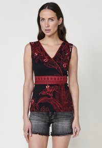 Top senza maniche nero con un motivo floreale rosso, scollo a V e fascia decorativa in vita. Abbinato a pantaloni shorts in denim.