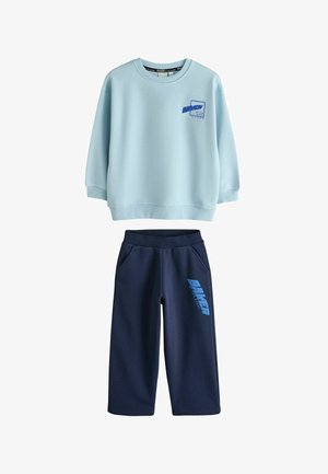 Felpa a maniche lunghe azzurro chiaro con logo "Baker" sul petto, abbinata a pantaloni blu scuro con la scritta "Baker" sulla coscia sinistra.