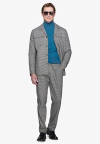 Szary garnitur w wzór houndstooth z dopasowaną marynarką, pasującymi spodniami oraz niebieskim golfem, dopełniony czarnymi okularami przeciwsłonecznymi i butami.