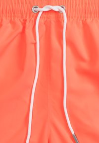 Neon pomarańczowe kąpielówki z elastycznym pasem, białym sznurkiem i srebrnymi oczkami, charakteryzujące się gładką, wodoodporną fakturą.