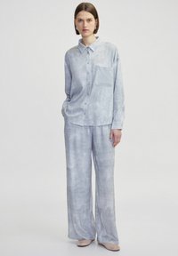Camisa abotonada de textura gris claro con un bolsillo, combinada con pantalones de pierna ancha, ambos con un patrón suave y sutil y un ajuste relajado.