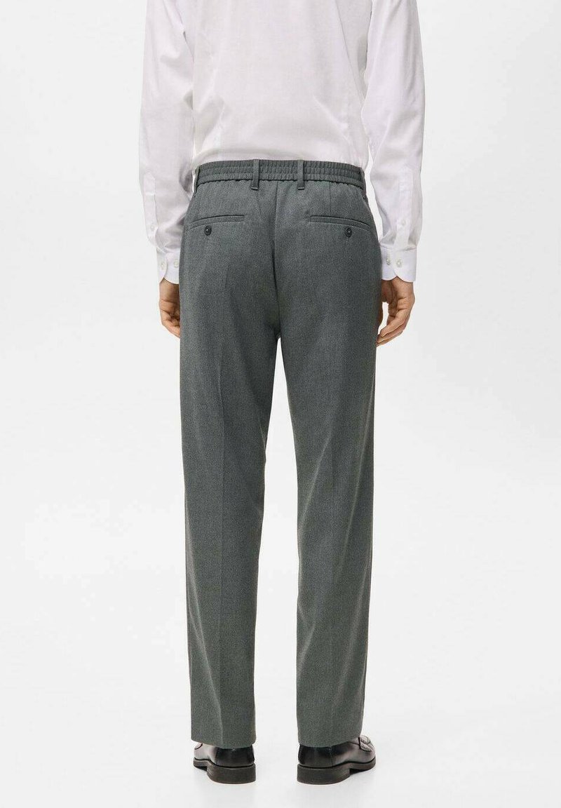 Grau maßgeschneiderte Hose mit strukturierter Oberfläche, elastischem Bund und zwei Gesäßtaschen. Kombiniert mit einem weißen Hemd und schwarzen Schuhen.