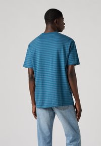 T-shirt azul-turquesa com riscas, de corte descontraído, mangas curtas e decote redondo, combinada com jeans azul claro. Material em algodão.