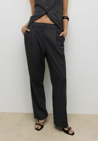 Czarne, dopasowane spodnie z wysokim stanem, zakładkami i bocznymi kieszeniami, wykonane z gładkiej tkaniny. Do tego czarne sandały z paskami.